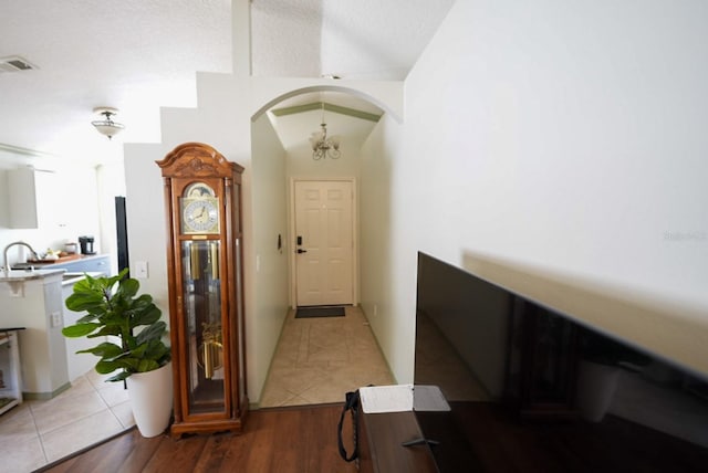 hallway featuring arched walkways, light tile patterned flooring, a sink, and lofted ceiling