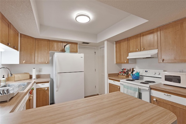 kitchen with under cabinet range hood, white appliances, a sink, and a tray ceiling