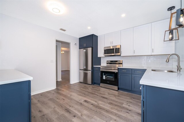 713 Coach Light Dr, Fern Park, FL 32730 - kitchen featuring appliances with stainless steel finishes, blue cabinetry, a sink, light wood-type flooring, and decorative backsplash