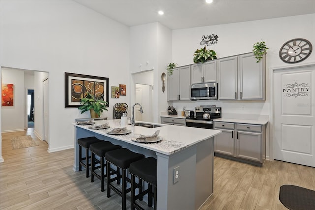 kitchen with appliances with stainless steel finishes, a sink, gray cabinets, a high ceiling, and a breakfast bar