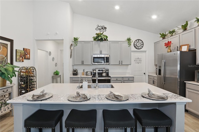 kitchen featuring stainless steel appliances, a breakfast bar area, light countertops, light wood-style flooring, and high vaulted ceiling