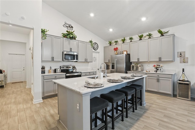 kitchen featuring appliances with stainless steel finishes, a sink, gray cabinetry, a kitchen bar, and light wood-style floors