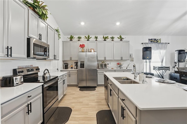 kitchen featuring stainless steel appliances, a sink, light countertops, light wood-type flooring, and recessed lighting