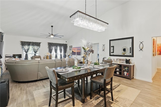 dining room with light wood finished floors, high vaulted ceiling, ceiling fan, baseboards, and a chandelier