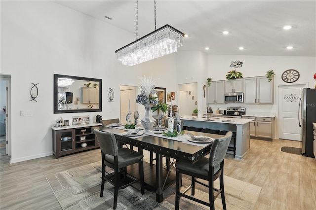 dining space with a towering ceiling, light wood-type flooring, a chandelier, baseboards, and recessed lighting