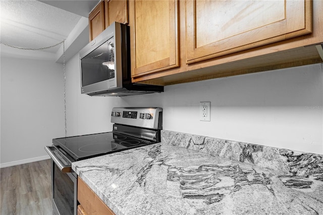 1163 Paseo Del Mar Unit B, Casselberry, FL 32707 - kitchen with stainless steel appliances, light wood-type flooring, light stone counters, baseboards, and brown cabinetry