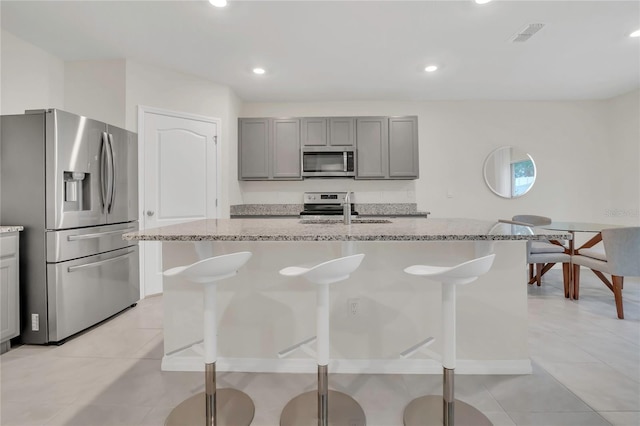 kitchen with stainless steel appliances, a sink, gray cabinetry, light stone counters, and recessed lighting