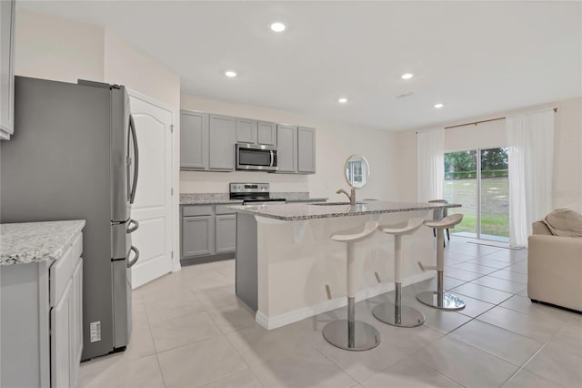 kitchen featuring stainless steel appliances, gray cabinets, a sink, light stone counters, and recessed lighting