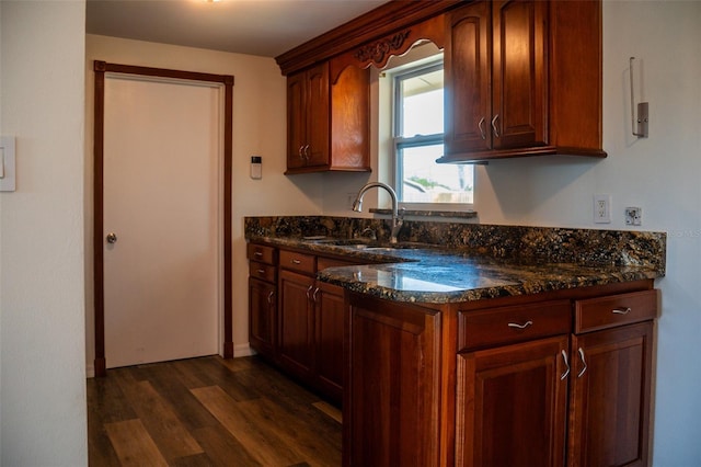 kitchen featuring dark wood-style flooring, dark stone counters, a sink, and baseboards