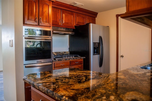 kitchen with under cabinet range hood, stainless steel appliances, and dark stone countertops