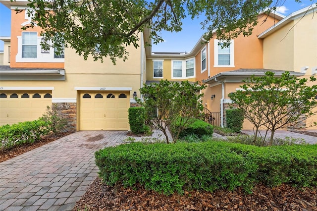 view of property with an attached garage, stucco siding, decorative driveway, and stone siding
