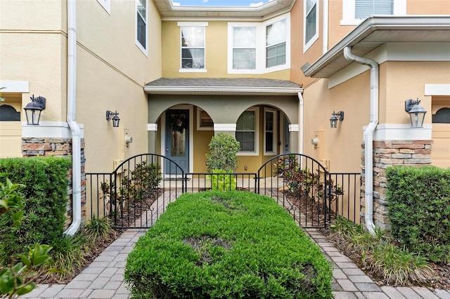 view of exterior entry featuring stucco siding, stone siding, fence, and covered porch