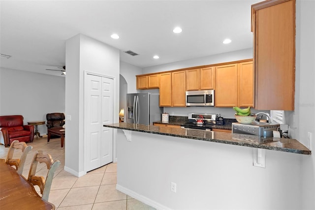 kitchen with appliances with stainless steel finishes, a peninsula, dark stone counters, light tile patterned floors, and recessed lighting