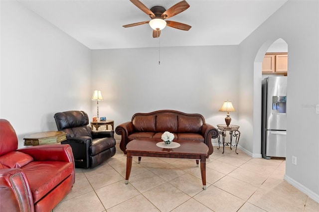 living room featuring a ceiling fan, arched walkways, light tile patterned floors, and baseboards