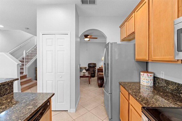kitchen with ceiling fan, light tile patterned floors, arched walkways, dark stone counters, and freestanding refrigerator