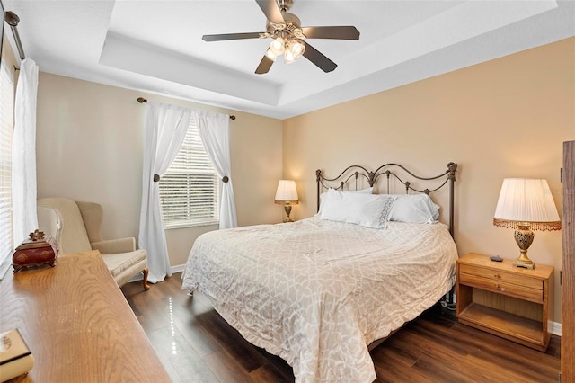 bedroom featuring a tray ceiling, wood finished floors, baseboards, and ceiling fan
