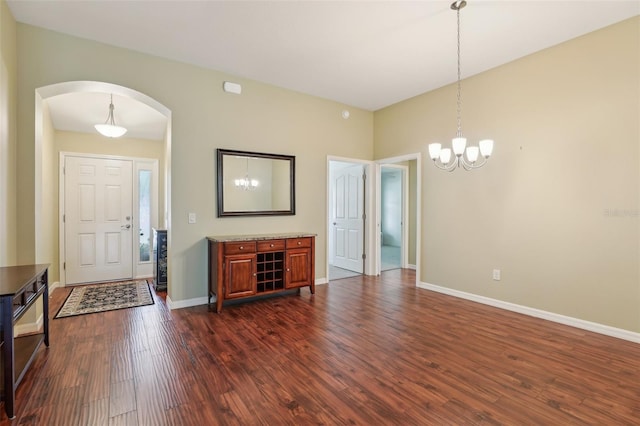 entryway with arched walkways, dark wood finished floors, a chandelier, and baseboards