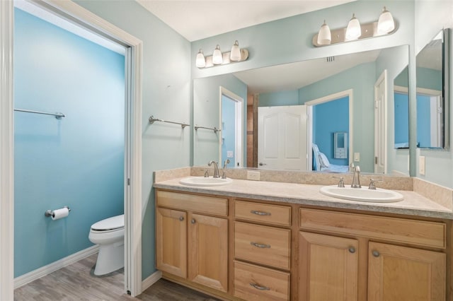bathroom featuring toilet, double vanity, wood finished floors, and baseboards