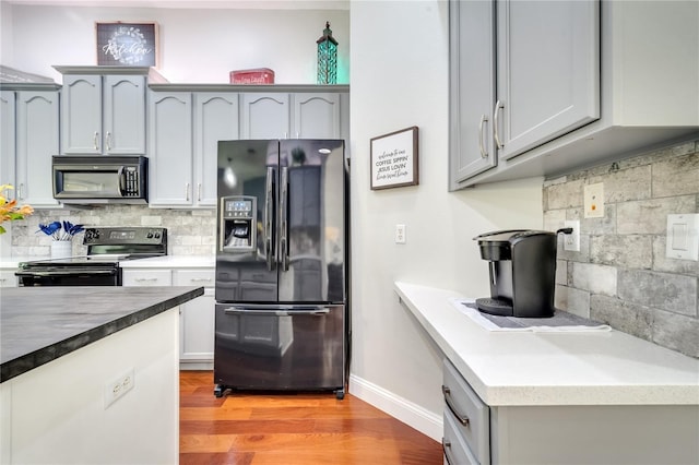 3380 Pawleys Loop N, Saint Cloud, FL 34769 - kitchen with black appliances, light wood finished floors, decorative backsplash, baseboards, and gray cabinetry
