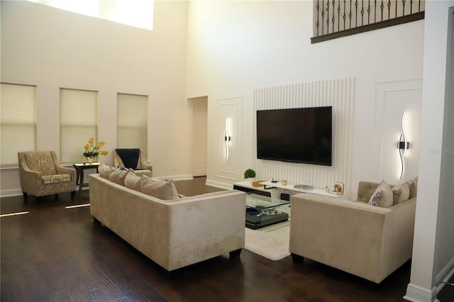 living room featuring a high ceiling, dark wood-type flooring, and baseboards