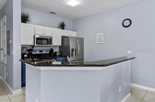 3193 Yellow Lantana Ln, Kissimmee, FL 34747 - kitchen featuring stainless steel appliances, light tile patterned flooring, dark countertops, white cabinets, and a textured ceiling