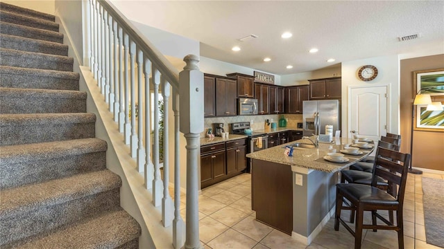 2030 Majorca Dr, Kissimmee, FL 34747 - kitchen featuring stainless steel appliances, dark brown cabinetry, a kitchen bar, light stone countertops, and recessed lighting