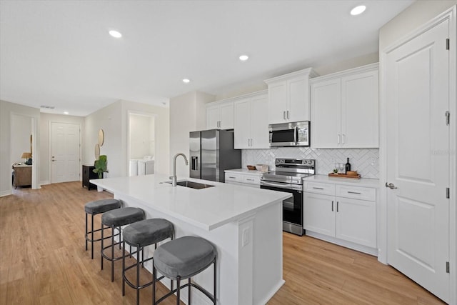 kitchen with stainless steel appliances, a sink, a kitchen bar, an island with sink, and backsplash