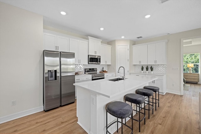 kitchen featuring appliances with stainless steel finishes, a sink, a kitchen breakfast bar, a kitchen island with sink, and white cabinetry