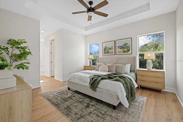 bedroom featuring a tray ceiling, light wood-style flooring, baseboards, and multiple windows