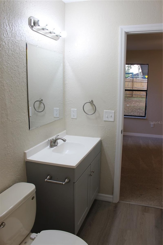 half bathroom with toilet, vanity, wood finished floors, baseboards, and a textured wall