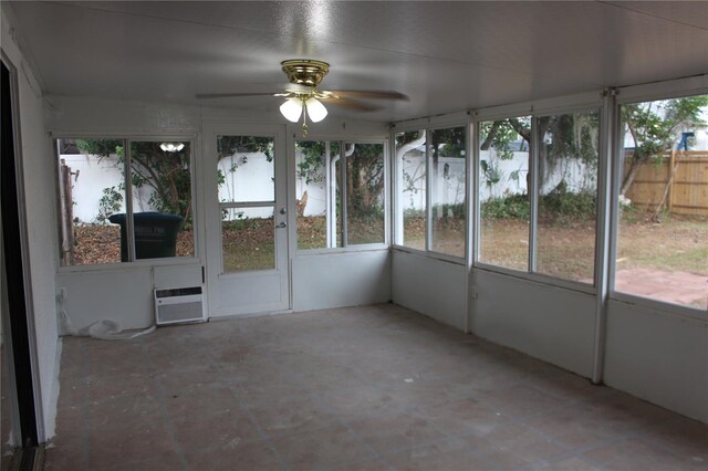 unfurnished sunroom featuring plenty of natural light, a ceiling fan, and a wall unit AC
