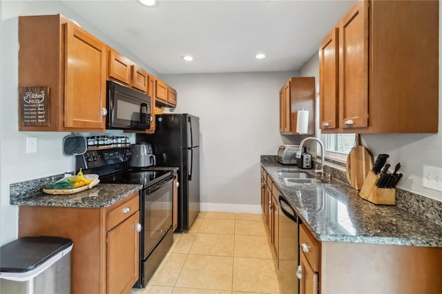 kitchen featuring black appliances, a sink, brown cabinetry, baseboards, and dark stone countertops