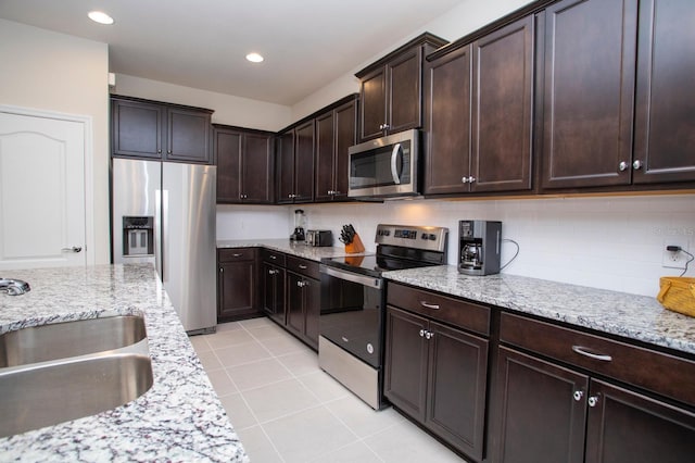 8944 Sydney Ave, Kissimmee, FL 34747 - kitchen featuring stainless steel appliances, a sink, light stone countertops, dark brown cabinetry, and light tile patterned floors