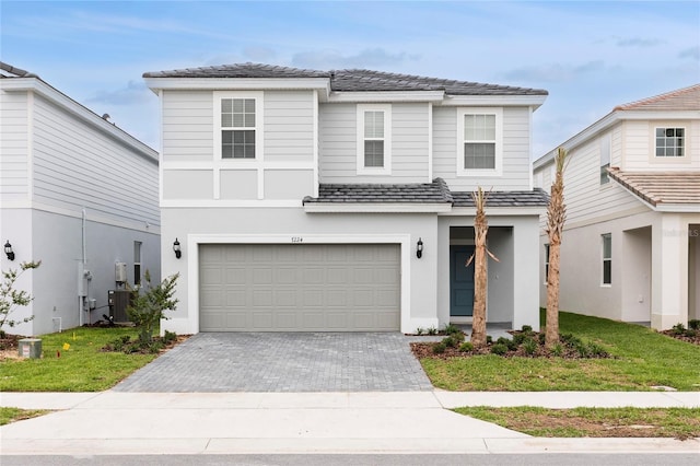 traditional-style house with a garage, decorative driveway, central AC unit, and stucco siding