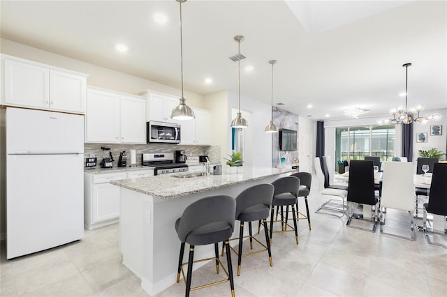 kitchen featuring appliances with stainless steel finishes, a sink, decorative backsplash, an island with sink, and white cabinets