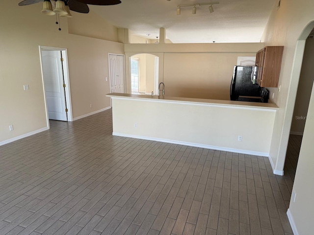 unfurnished living room featuring arched walkways, a ceiling fan, baseboards, dark wood-style flooring, and a sink