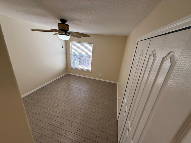 unfurnished bedroom with a textured ceiling, baseboards, ceiling fan, a closet, and dark tile patterned floors