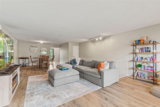 living area featuring light wood finished floors, track lighting, plenty of natural light, and a textured ceiling