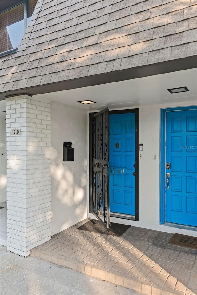 view of exterior entry with roof with shingles and stucco siding