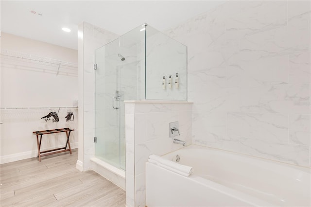 full bathroom featuring a stall shower, a bath, a walk in closet, wood finished floors, and baseboards