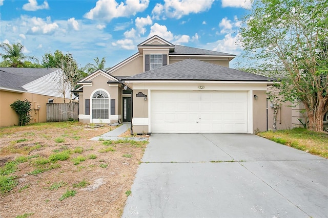 traditional-style home featuring an attached garage, concrete driveway, stucco siding, a shingled roof, and fence