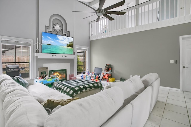 tiled living room with a towering ceiling, a ceiling fan, a glass covered fireplace, and healthy amount of natural light