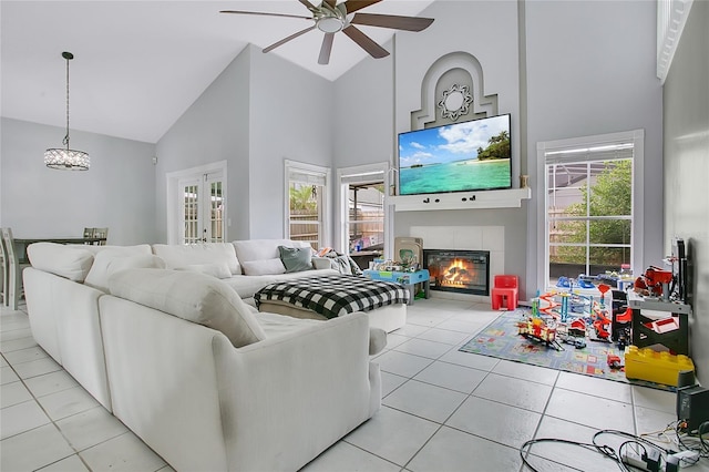 living room with high vaulted ceiling, ceiling fan, light tile patterned floors, a tile fireplace, and healthy amount of natural light