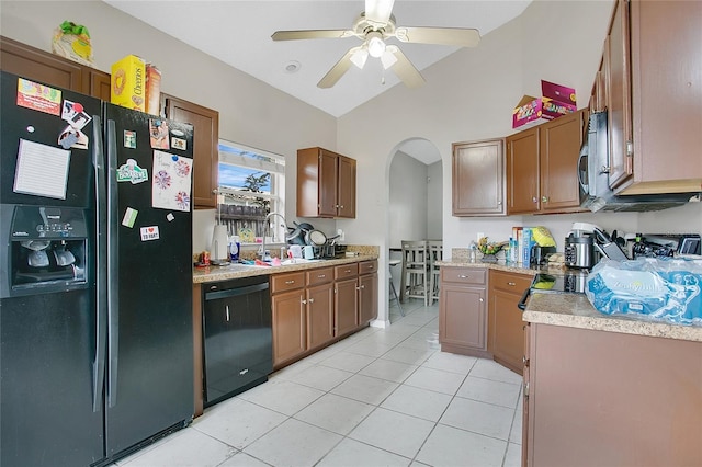 kitchen featuring black appliances, arched walkways, light tile patterned floors, a sink, and light countertops