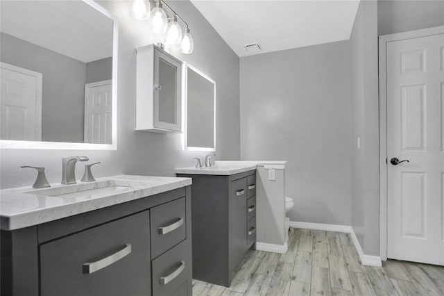 full bathroom with wood finished floors, two vanities, toilet, and baseboards