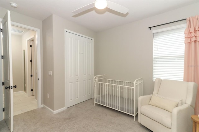 bedroom featuring carpet flooring, a closet, ceiling fan, a crib, and baseboards
