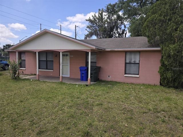 rear view of property featuring concrete block siding, a lawn, a patio, and roof with shingles