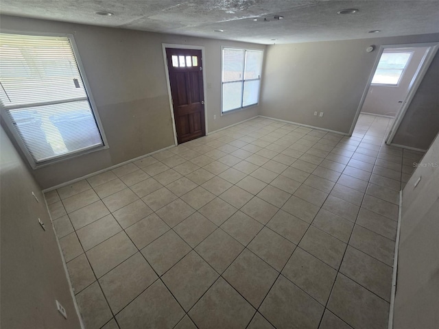 entrance foyer with light tile patterned floors, healthy amount of natural light, baseboards, and a textured ceiling