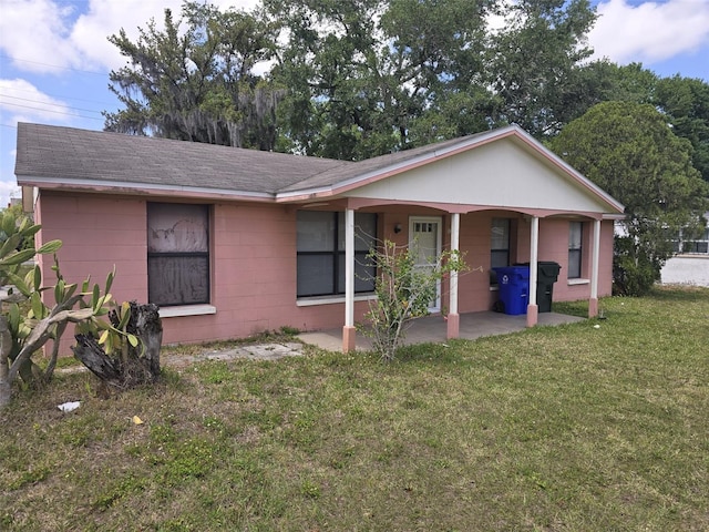 ranch-style house featuring concrete block siding, a front lawn, roof with shingles, and a patio