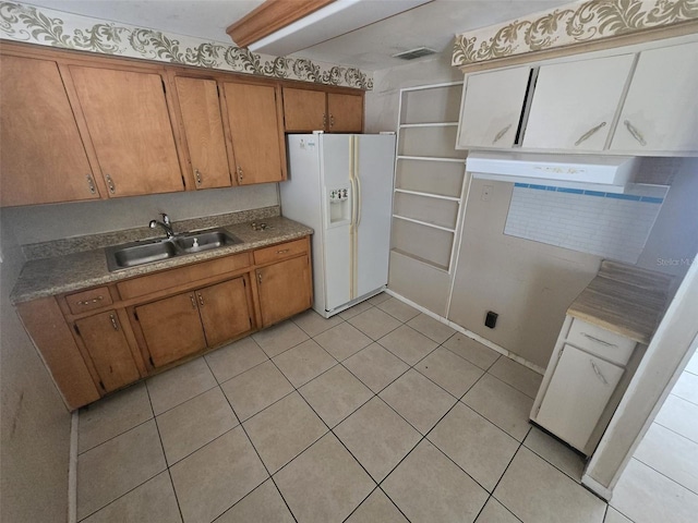 kitchen featuring white fridge with ice dispenser, a sink, brown cabinetry, and light tile patterned floors